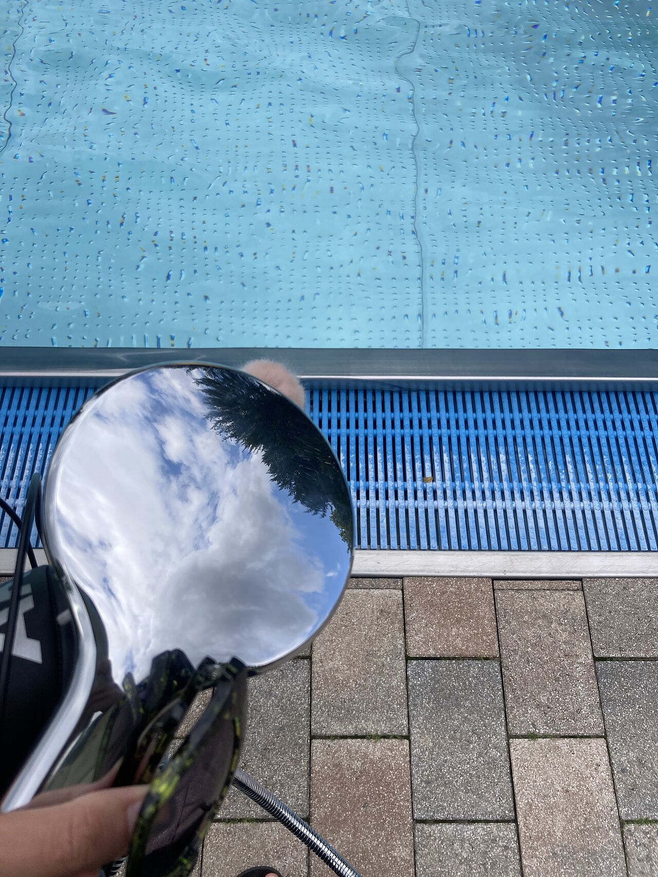 [Translate to English:] Makroaufnahme eines Duschkopfes, der zum Mikrofon umfunktioniert ist. Er schaut auf den Beckenrand einen Schwimmbeckens.
