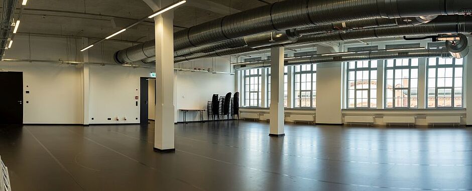 View of the rehearsal room with black dance floor, two pillars in the centre of the room and light-flooded window front.